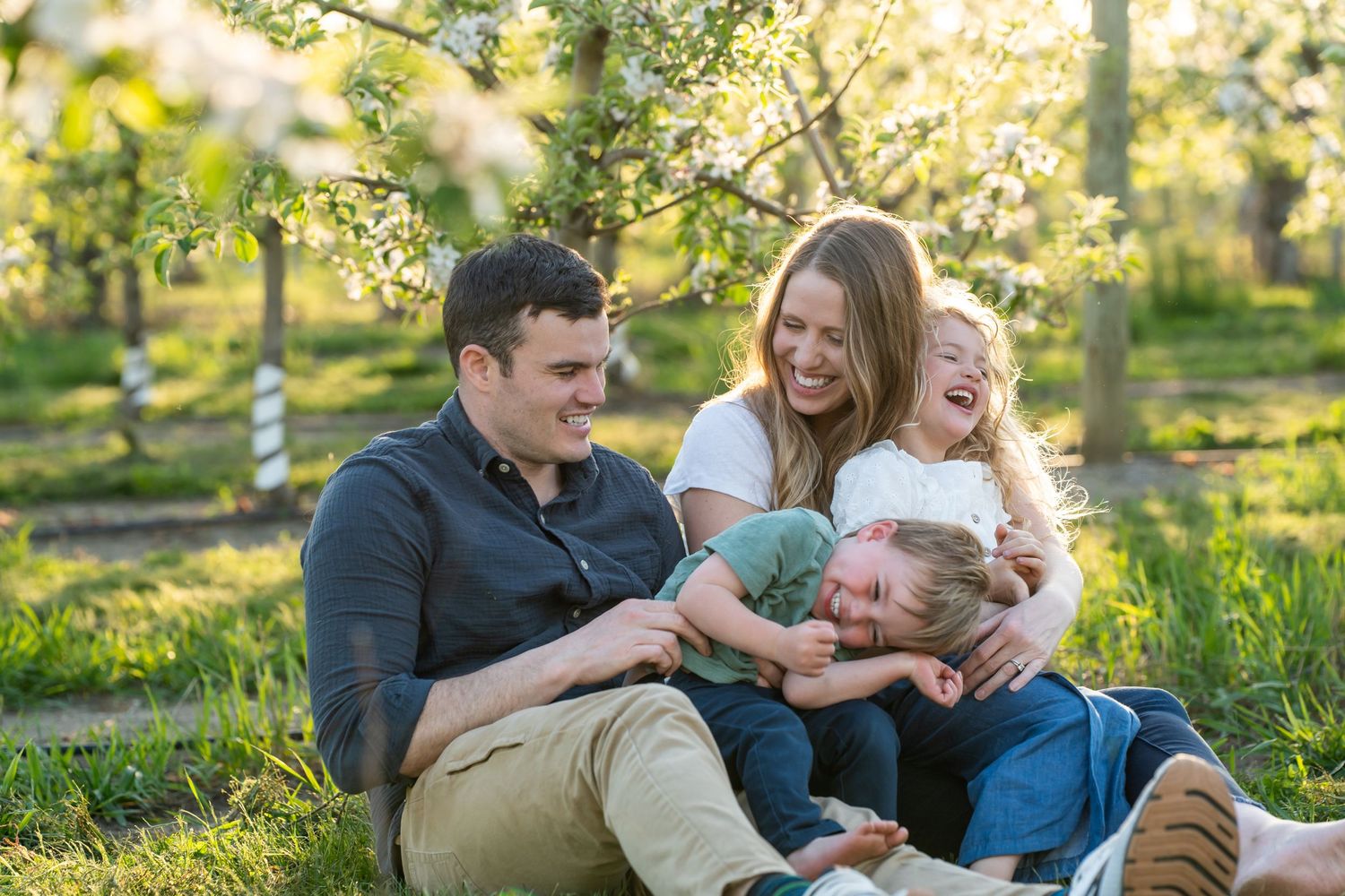 A happy couple in casual attire lounges together on a grassy lawn during golden hour.