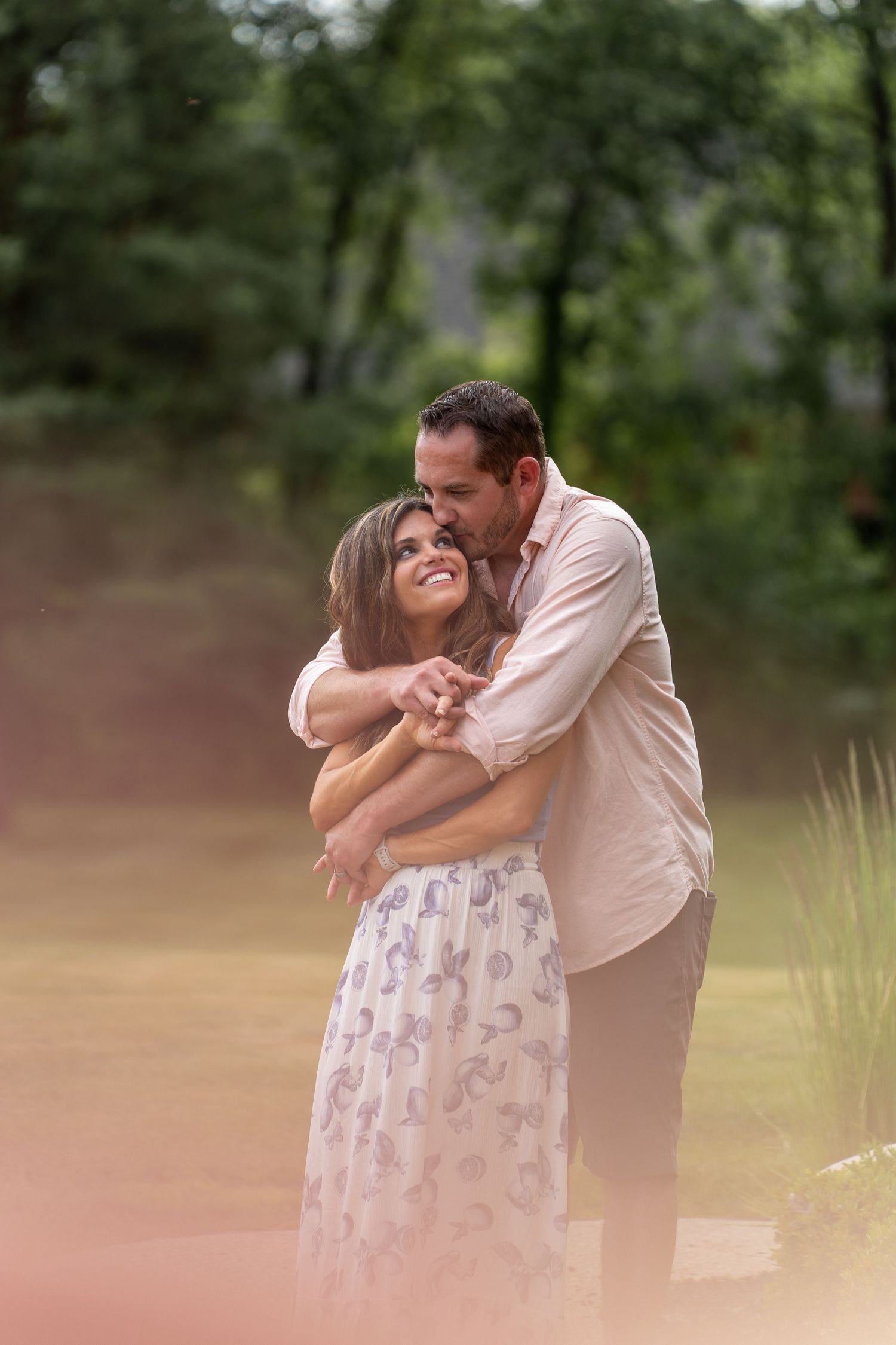 A romantic couple embraces tenderly in the park while enjoying a sweet kiss against a blurred natural background.