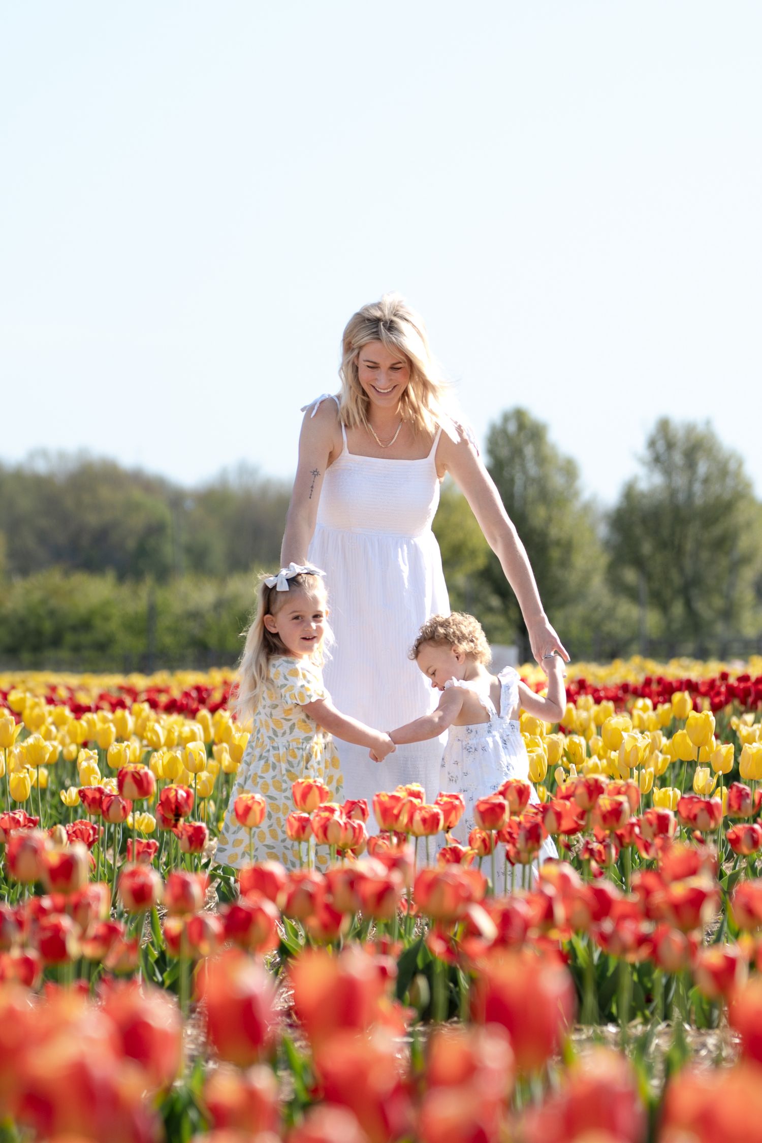 Two people stroll through a vibrant tulip field filled with red, yellow and orange flowers on a sunny spring day.