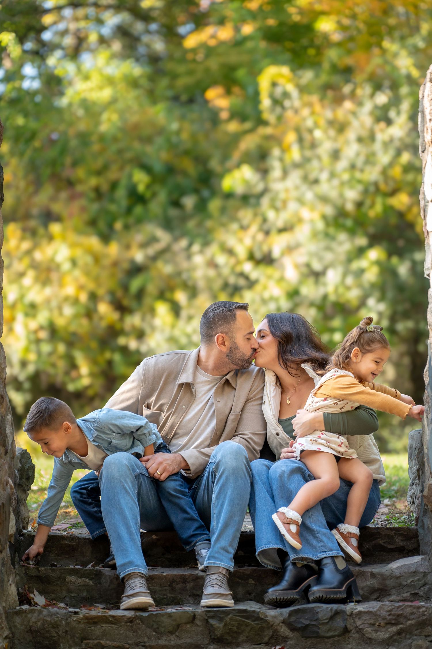 Four sequential photos show a couple sharing romantic kisses while sitting on a rustic stone wall in an autumn setting.