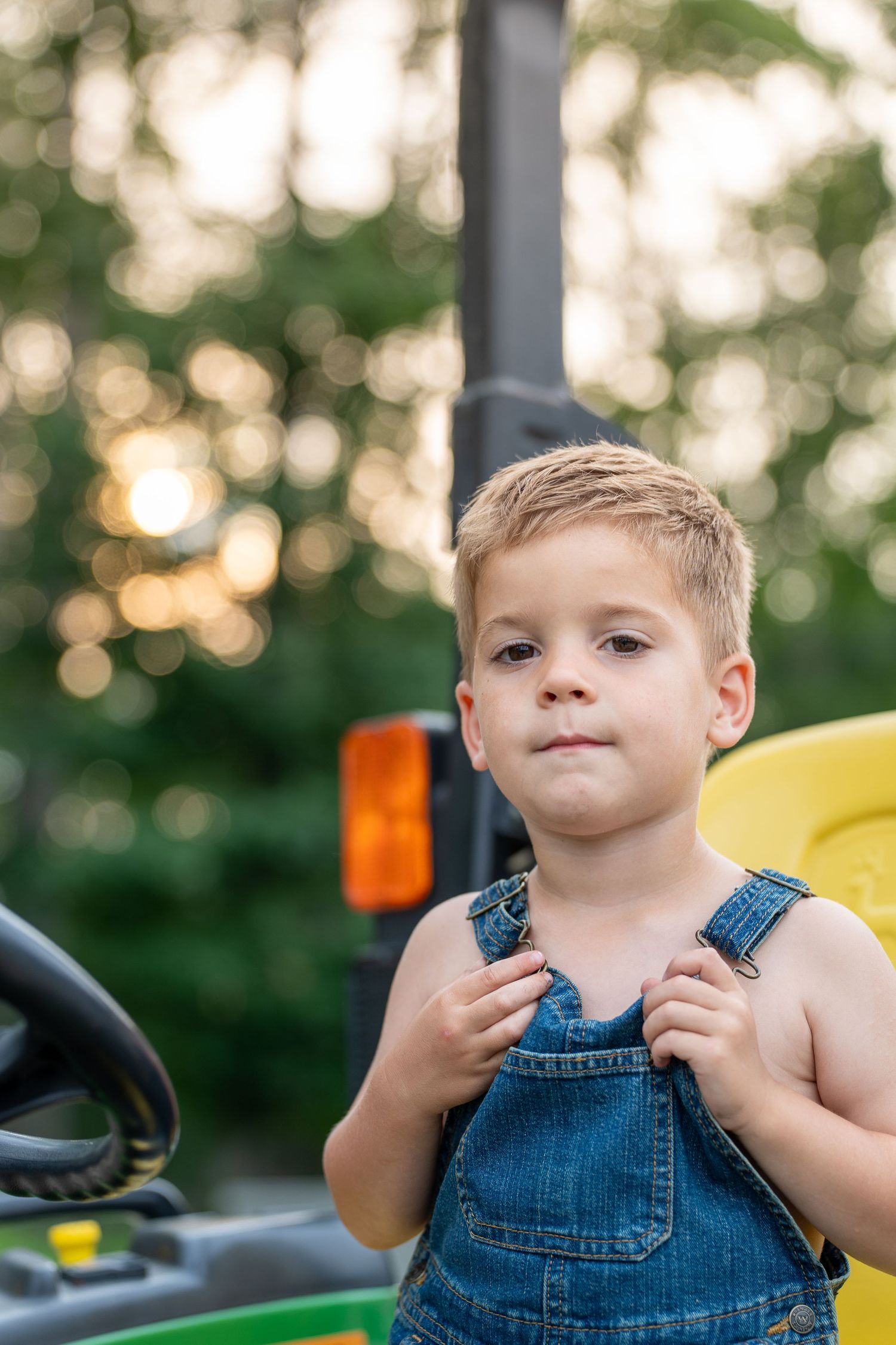 Child in denim overalls plays outdoors on playground equipment at sunset with blurred background.