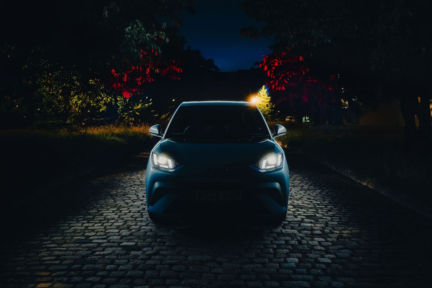 A BYD Dolphin Surf headlights illuminate a dark cobblestone street at night, creating a dramatic scene.