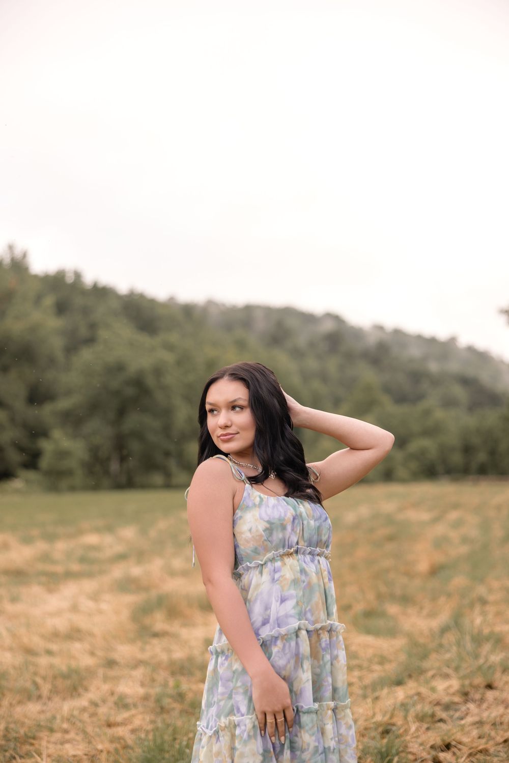 Someone wearing a floral tiered dress poses in a golden field with rolling hills in the background at sunset.