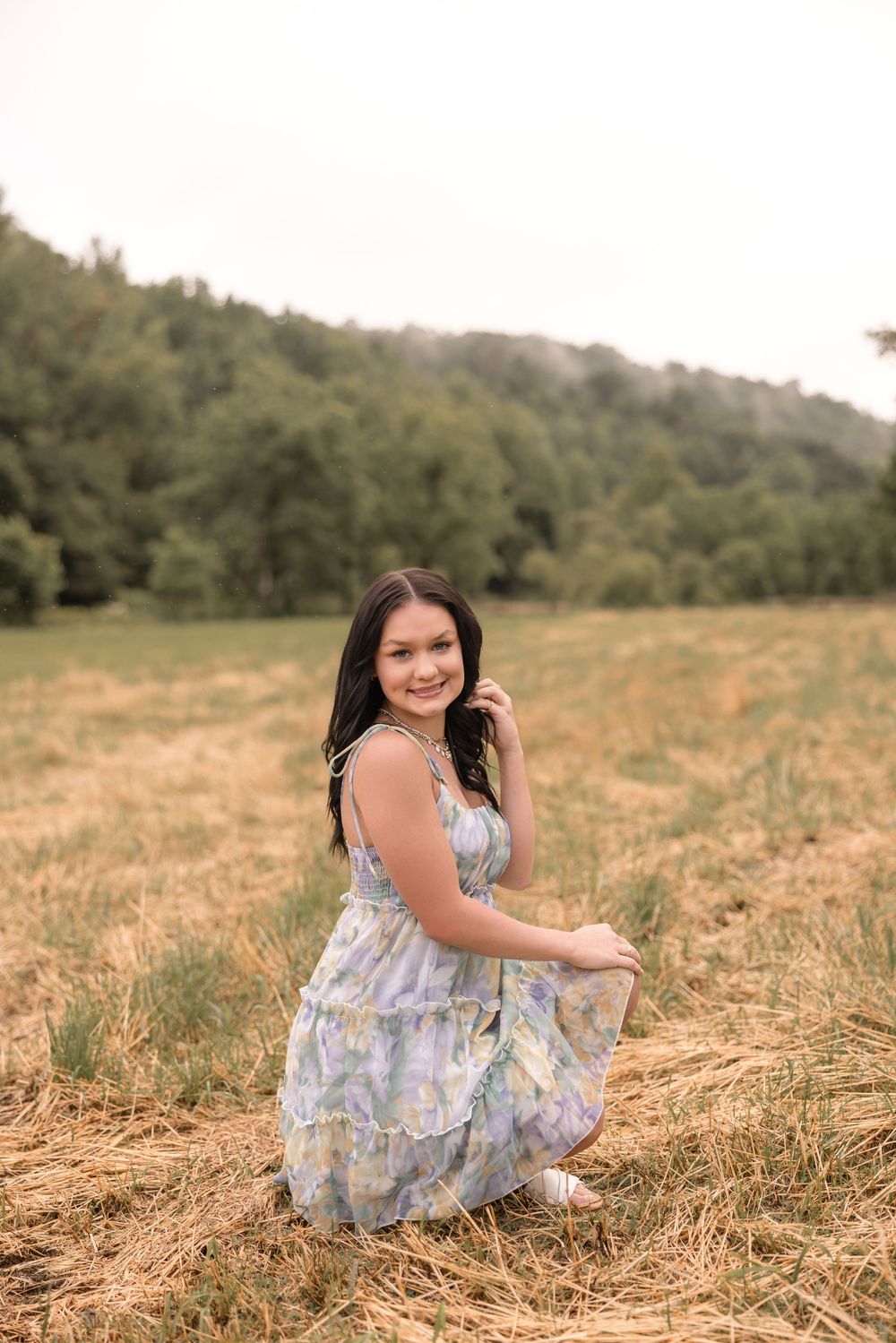 A person in a blue floral dress sits in a golden grassy field on a sunny afternoon.