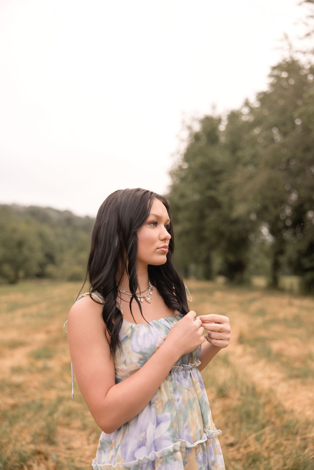 Woman wearing a blue and white sundress stands in a golden field during a summer photoshoot.