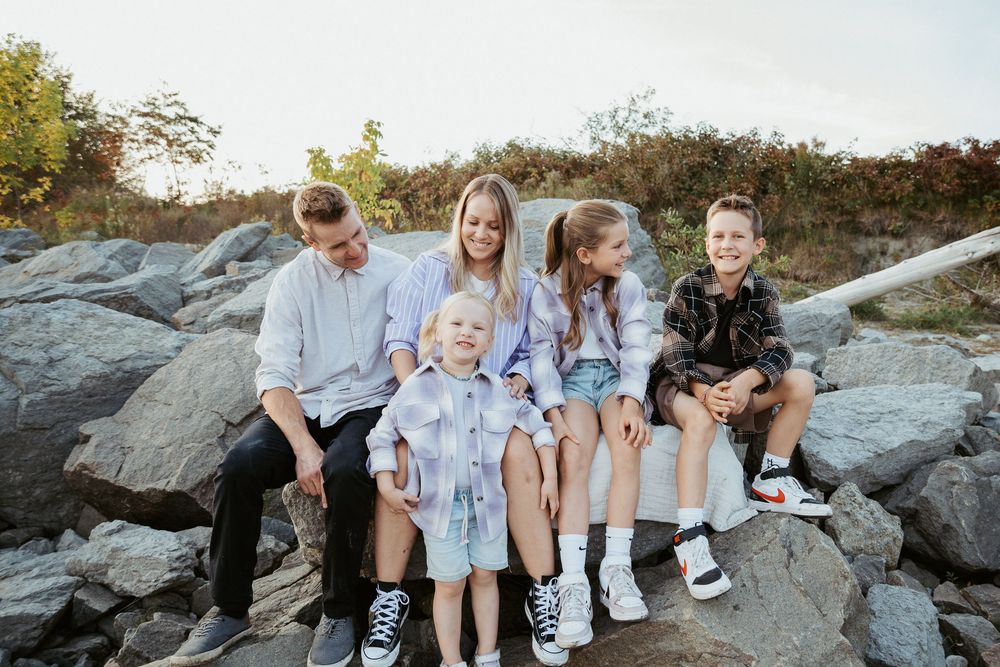 Family sitting together on large coastal rocks during a beach photoshoot.
