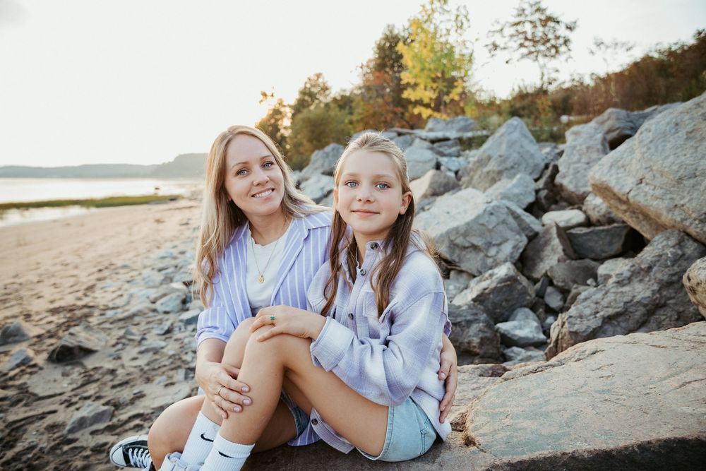 Two people sitting and smiling on rocky beach during sunset photoshoot.