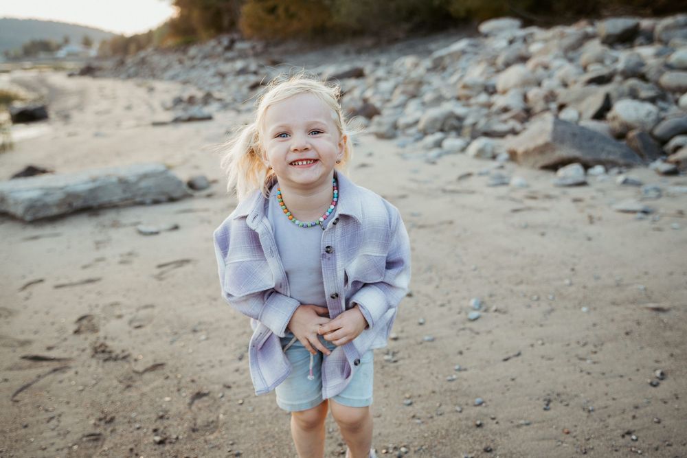 Young child in oversized blue shirt playing on a beach with rocks.