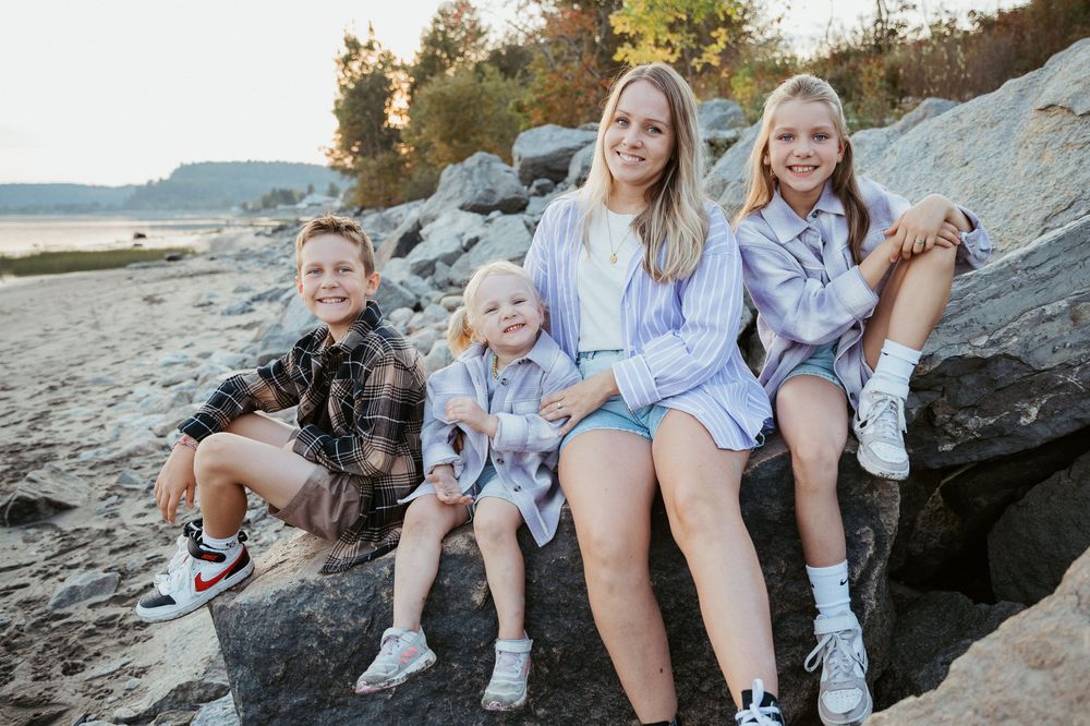 Family group seated on rocky beach outcropping during sunset photo session.