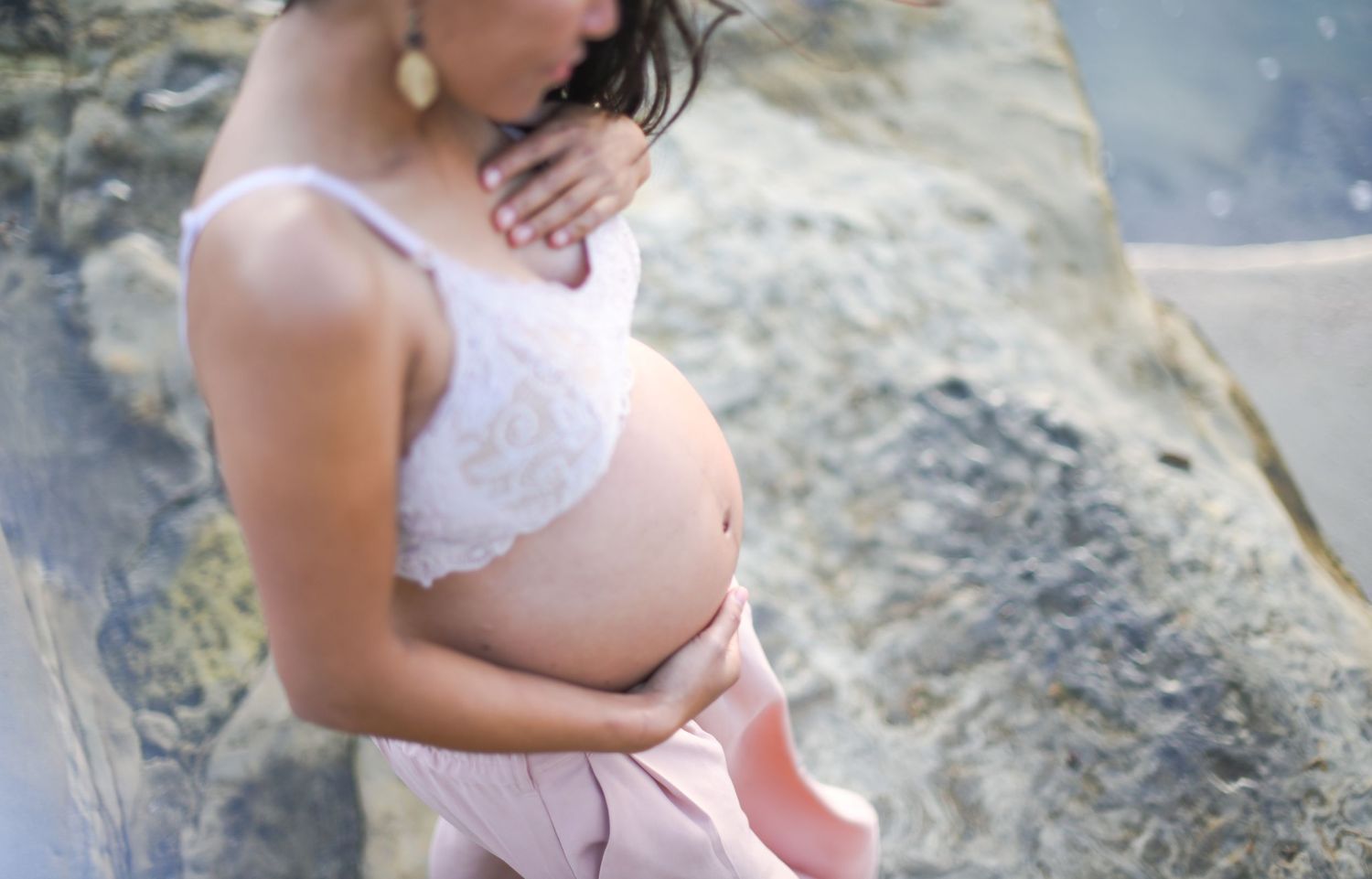 A maternity photo taken outdoors showing a pregnant belly in white lace against a natural rocky background.