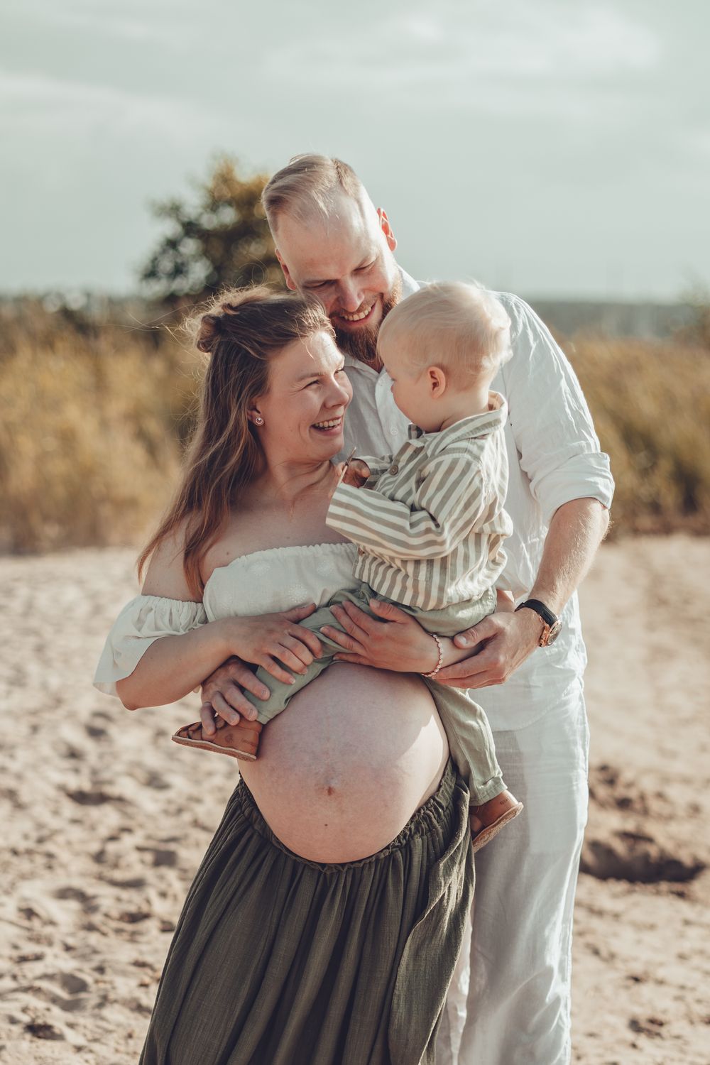 Happy pregnant woman with her husband and toddler son enjoying a family moment on a sandy beach.