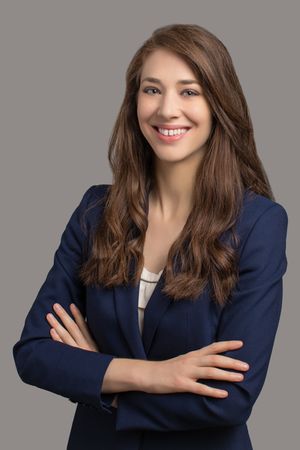 Professional headshot of a person in a navy blazer and white blouse smiling warmly against a gray background.