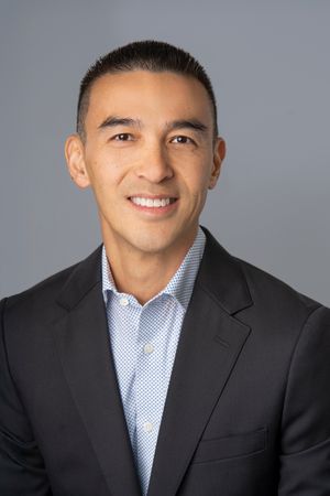 Professional headshot series showing a person in a black suit and light blue collared shirt against a gray backdrop.
