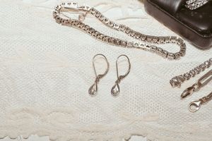 Delicate silver necklace and earrings displayed on white lace fabric with jewelry box in background.