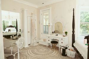 A bright white bedroom with four-poster bed, vintage vanity, and round jute rug on hardwood floors.