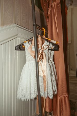 Several white lace wedding dresses and rose gold bridesmaid dresses hanging on clothing racks against a white wall.
