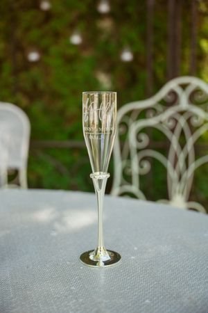 A crystal champagne flute sits elegantly on a white linen-covered table with ornate garden chairs in the background.