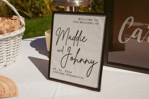 Rustic wedding decor features welcome signs and name cards arranged on white wicker baskets with elegant calligraphy.