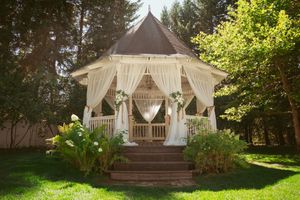 Romantic white gazebo decorated with flowing fabric and chandelier for an outdoor garden wedding ceremony.