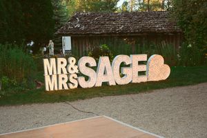 Large decorative 'Mr & Mrs SAGE' sign with heart displayed against rustic building.