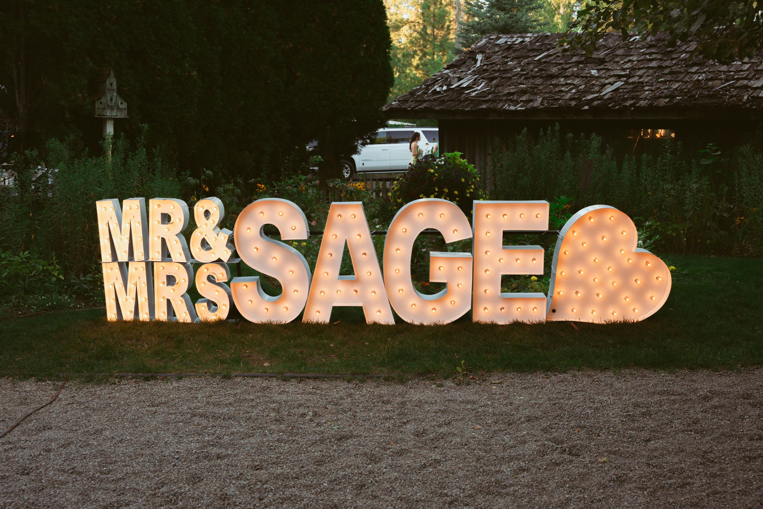 Illuminated 'Mr & Mrs SAGE' marquee letters with heart against dark background.