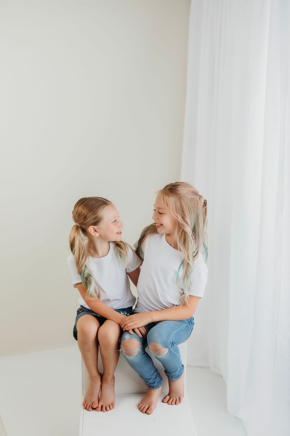 Children sit close together on white platform, laughing and bonding in matching white t-shirts.