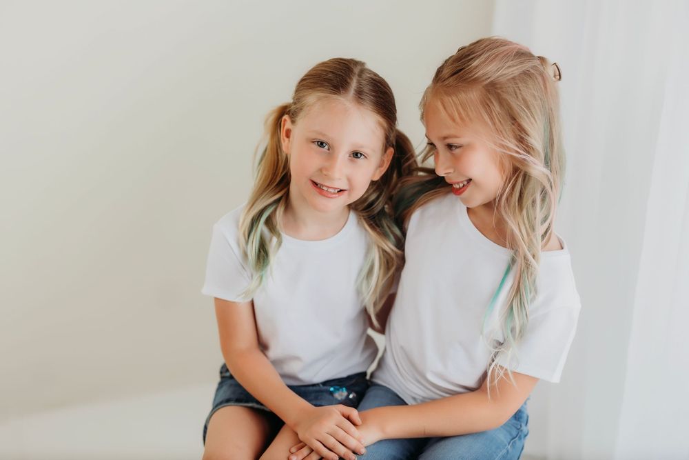 Children share candid laughter while sitting together in a bright white studio space.