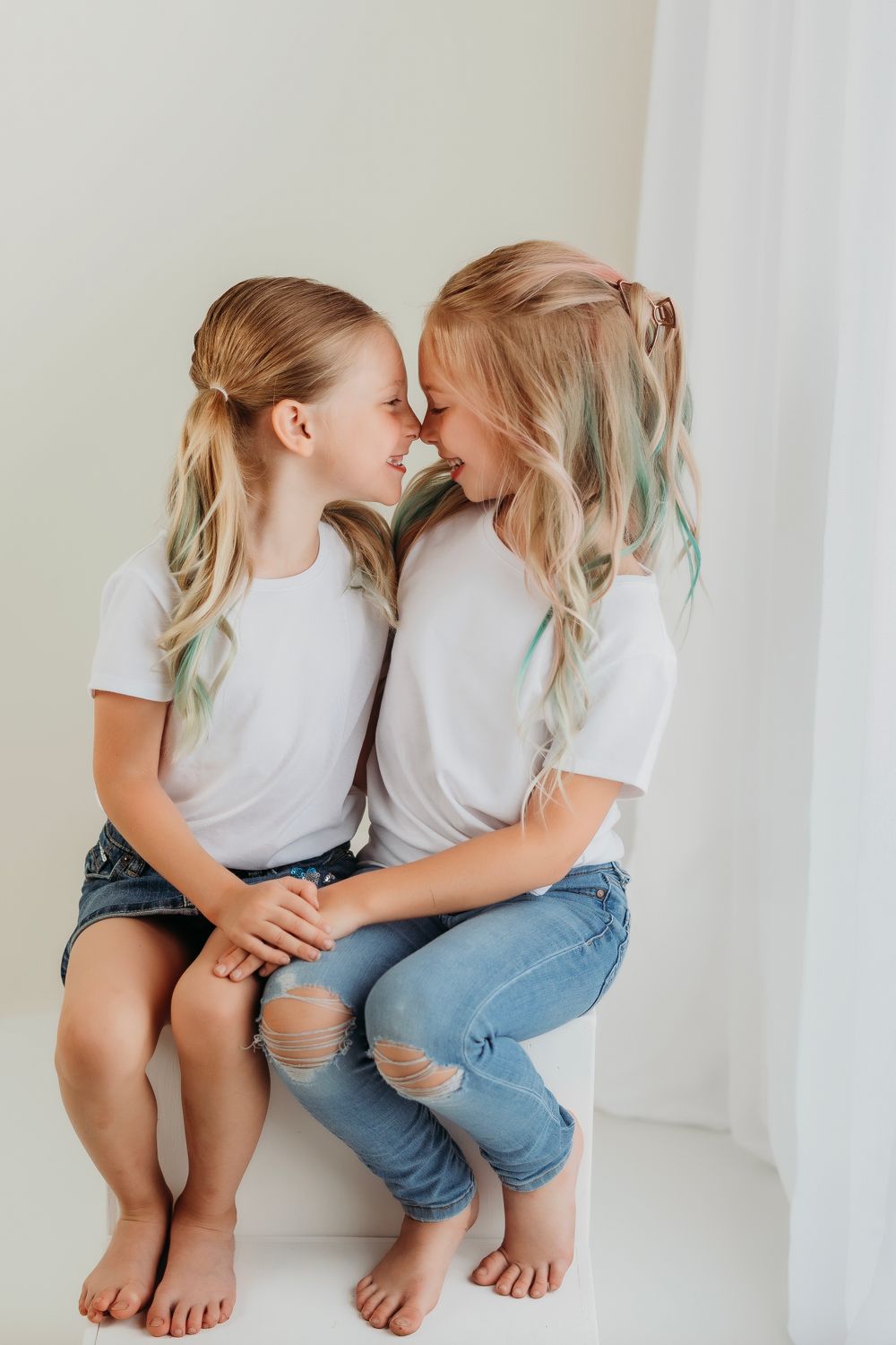 Two kids lean in close while sitting together, sharing an intimate moment against a white backdrop.