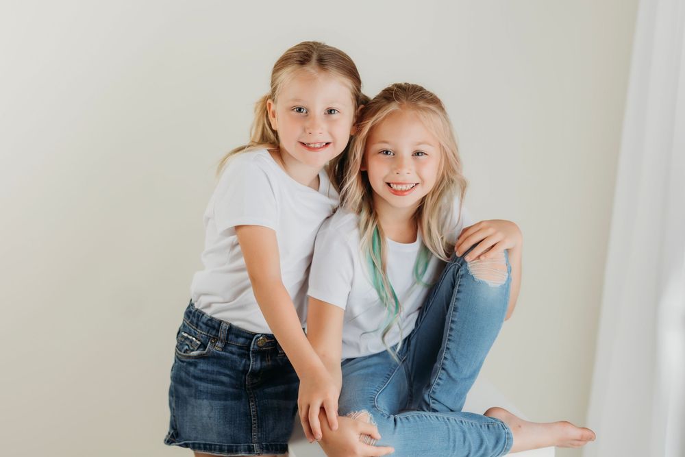 Two people in denim and white tops embrace while posing against a minimalist white background.