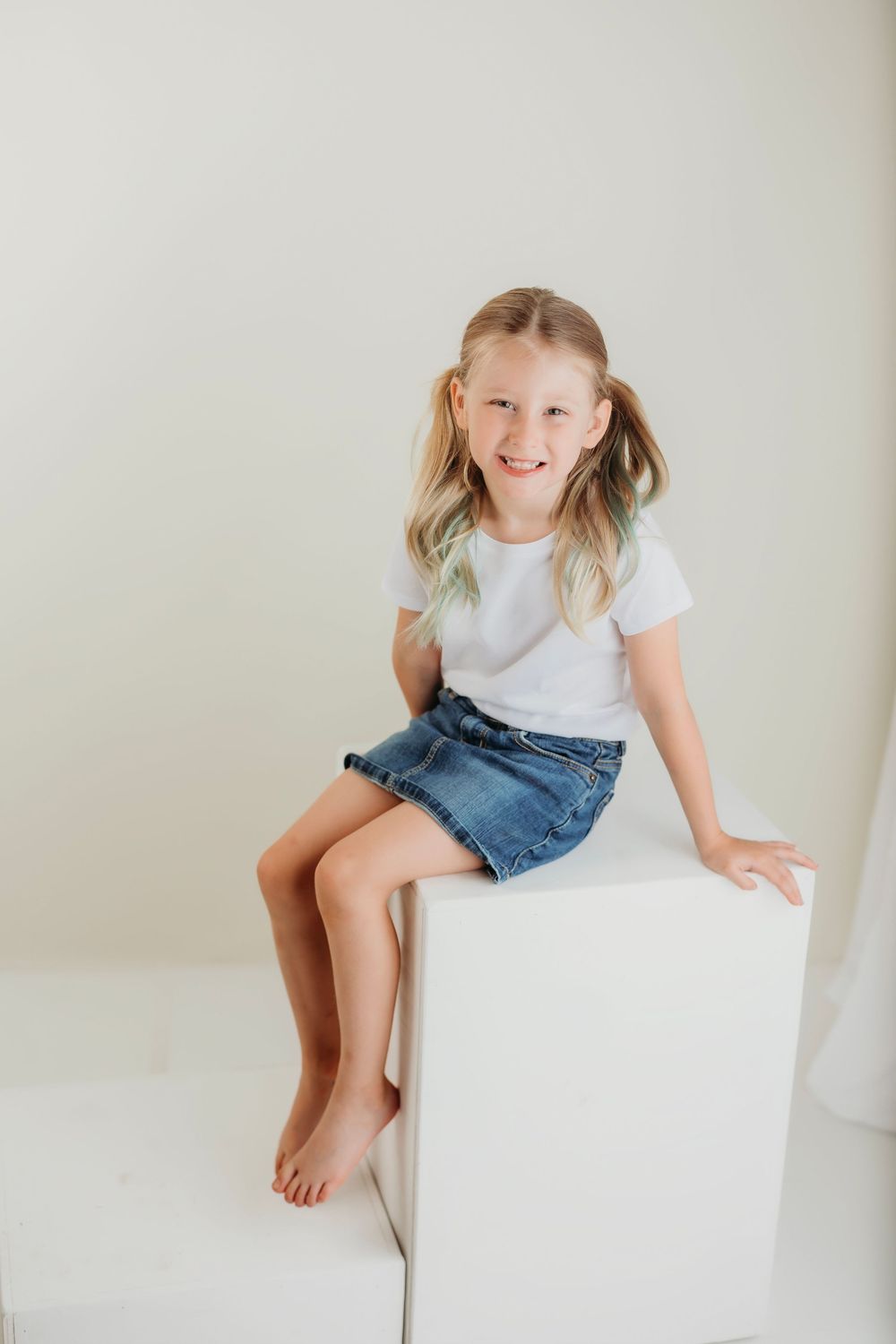 A young person in casual attire sits playfully on a white cube against a light background.
