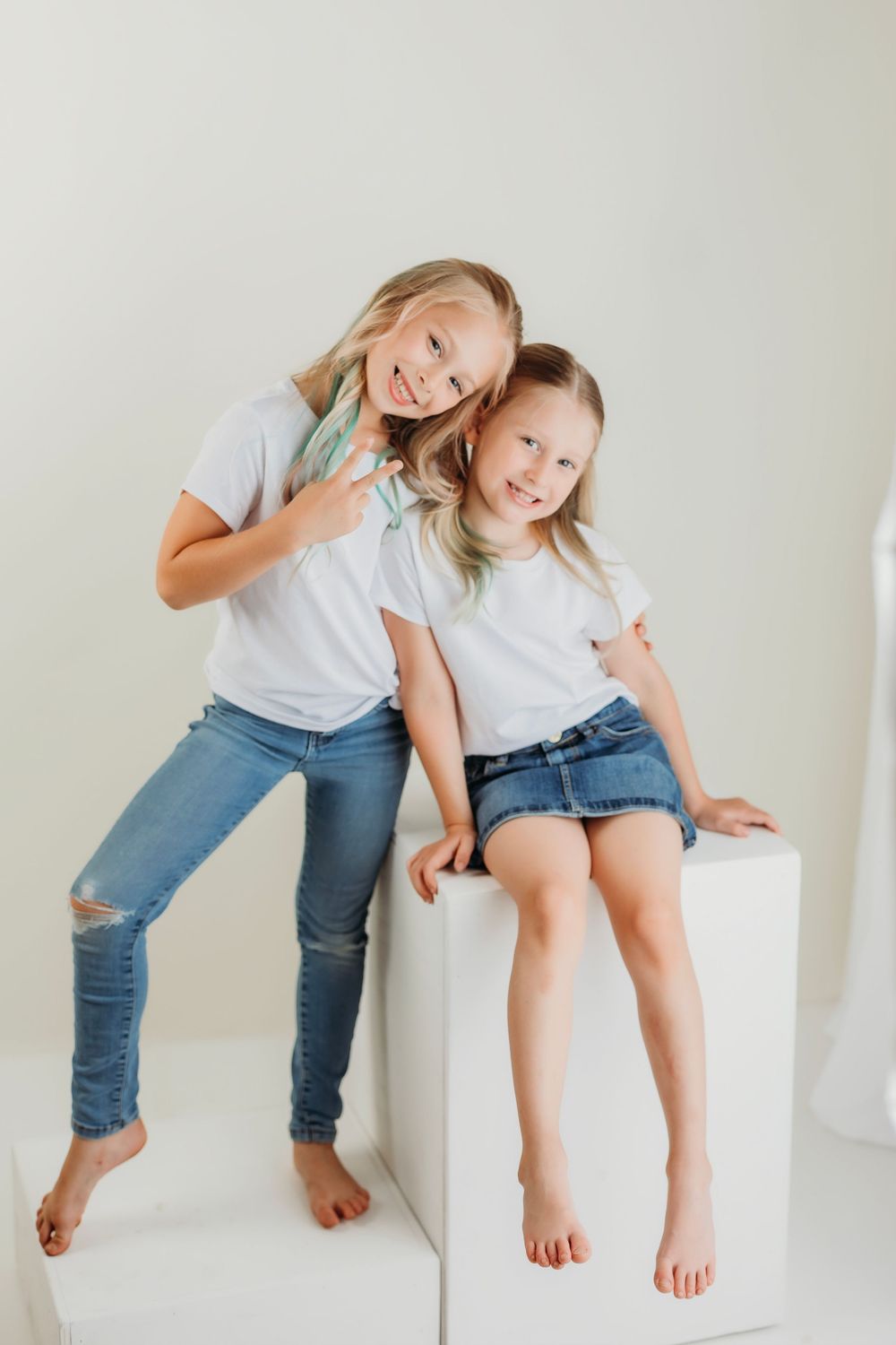 Two people in casual wear share a fun moment while posing by a white cube.