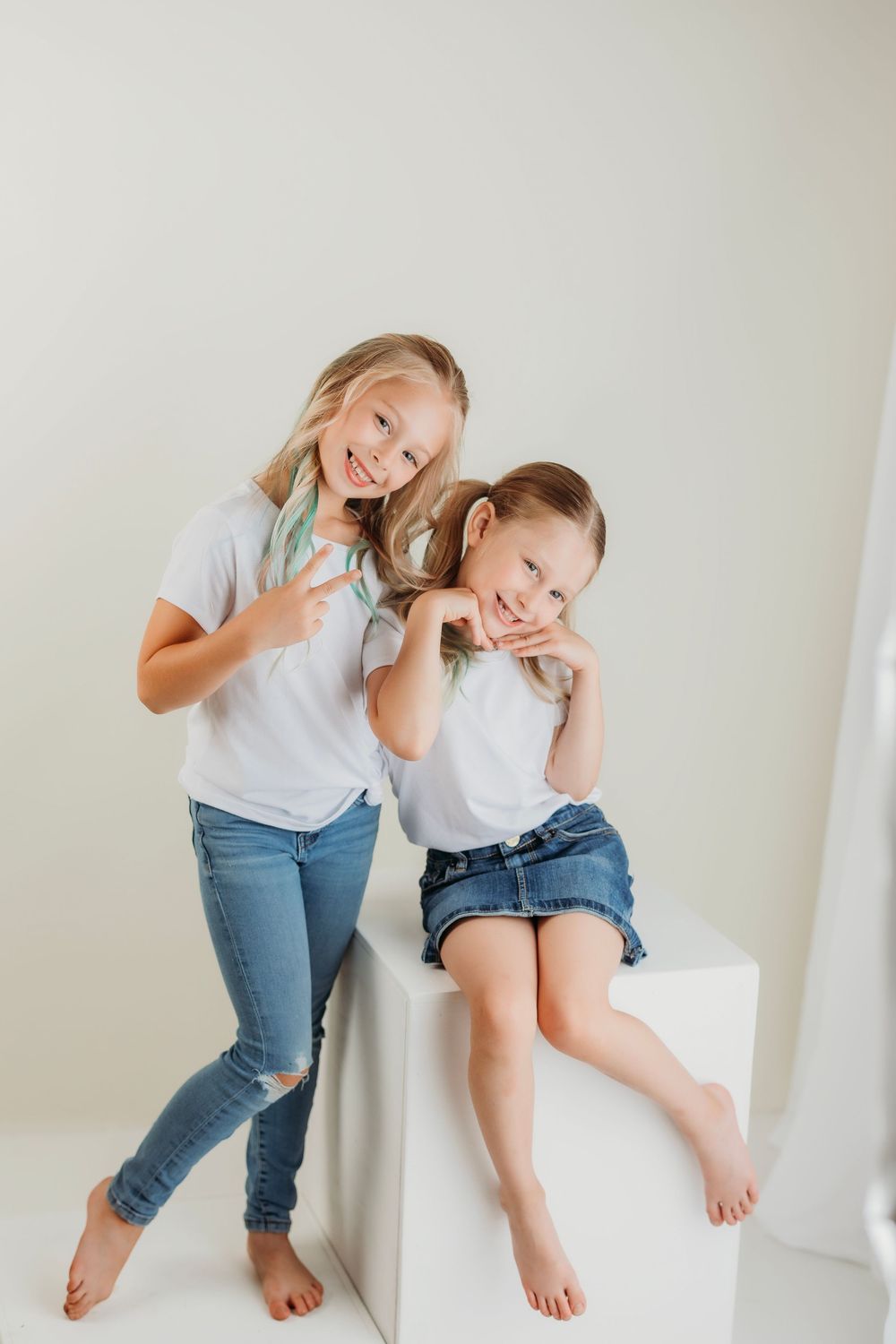 Two people in denim and white tops pose playfully together against a minimalist background.