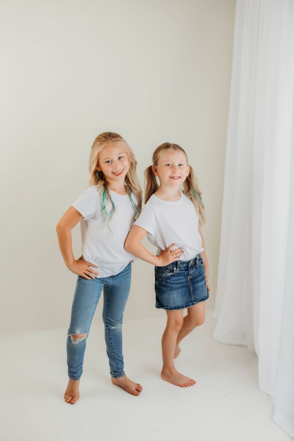 Two people in denim and white tops strike playful poses in a bright studio setting.