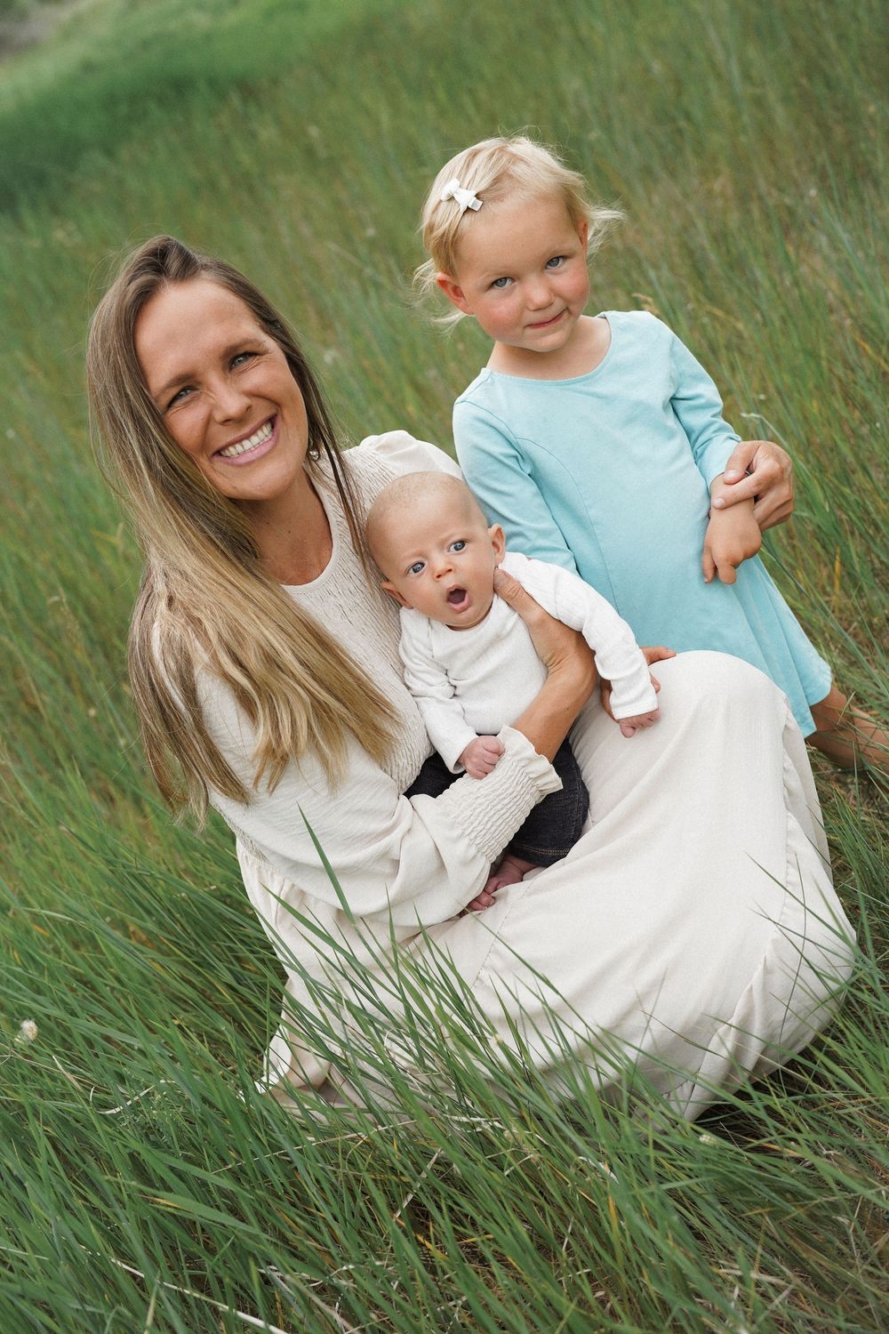 A joyful outdoor family portrait taken in tall green grass on a sunny day, capturing a tender moment together.