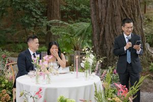 A wedding celebration in a redwood forest with elegant table settings and pink floral arrangements.