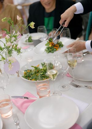 Elegant table setting at a wedding reception with white plates, wine glasses, and scattered floral decorations.