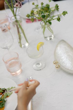 Delicate table setting with small glass vases holding fresh herbs and pink glassware.