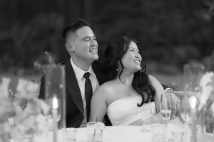 Black and white photo of couple laughing at reception with centerpieces visible on banquet table.