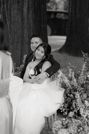 Two people in white attire share intimate embraces amidst blooming flowers in a romantic black and white photoshoot.