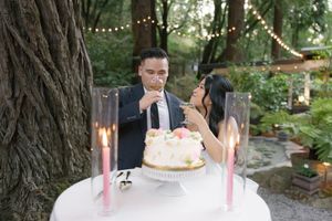 People celebrating with a birthday cake adorned with candles in an outdoor garden setting with string lights.