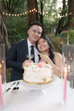 A wedding couple shares joyful moments together during their cake-cutting ceremony under string lights in an outdoor setting.