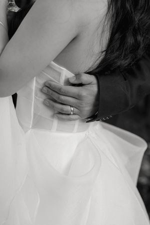 Black and white close-up photo showing hands adjusting a white wedding dress with ring visible.