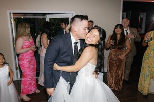 Wedding guests enjoy dancing and celebrating at an indoor reception venue with colorful dresses and decorations.