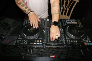 Close-up view of hands mixing music on DJ turntables and mixer equipment during a performance.