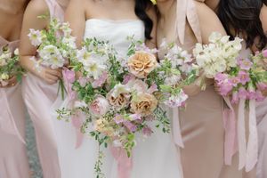 Wedding party holding beautiful bouquets with pink and peach roses, white flowers and delicate greenery.