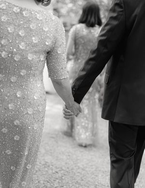 A close up black and white photograph capturing hands holding together during what appears to be a formal occasion.