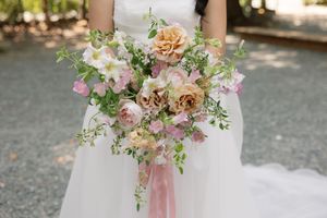 Wedding bouquet with peach roses, pink flowers and trailing green vines tied with soft pink ribbon.