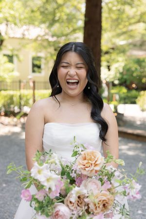 A stunning bridal portrait showcasing a joyful expression and beautiful peach and pink floral bouquet in an outdoor setting.