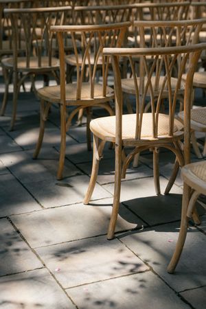 Wooden bistro chairs with curved backs cast shadows on stone tile flooring in natural sunlight.
