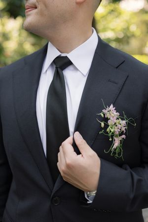 Close-up of formal black suit with white dress shirt, black tie and delicate purple floral boutonniere.